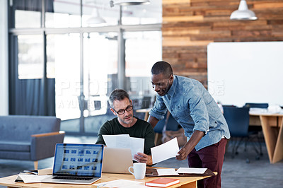 Buy stock photo Shot of two male coworkers discussing paperwork at a desk in an office