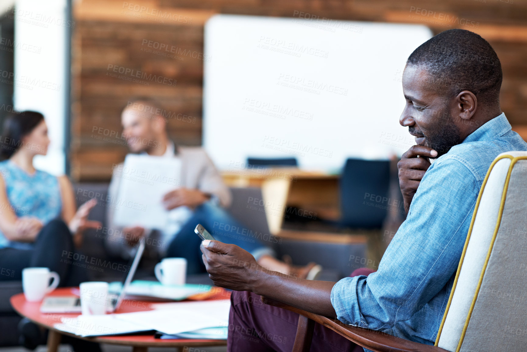 Buy stock photo Shot of a man texting with his colleagues blurred in the background