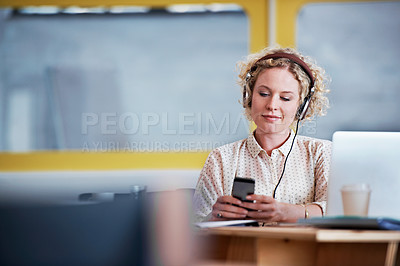 Buy stock photo Shot of a designer listening to music while texting at her desk