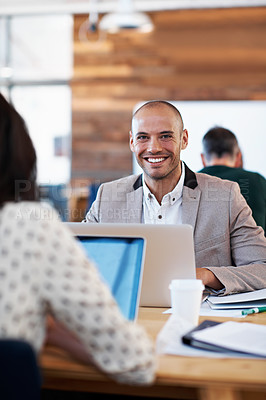 Buy stock photo Portrait of a handsome man sitting at his desk with his colleagues blurred out