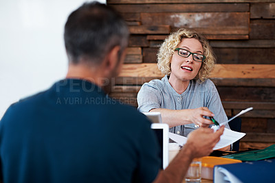 Buy stock photo Shot of two coworkers discussing paperwork at a desk in an office