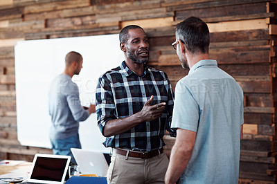 Buy stock photo Shot of two coworkers having a conversation with  their colleagues blurred in the background