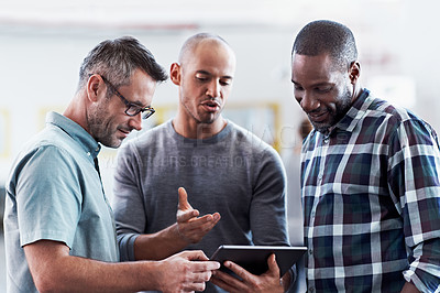 Buy stock photo Shot of three coworkers having a discussion over a digital tablet