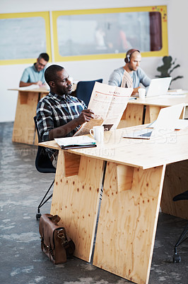 Buy stock photo Shot of a man reading a newspaper with his colleagues blurred in the background