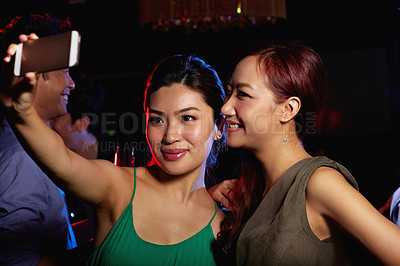 Buy stock photo Shot of a two attractive female friends taking a selfie in a nightclub