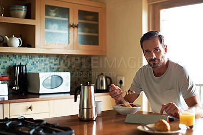 Buy stock photo Cropped shot of a handsome man eating breakfast while using a tablet