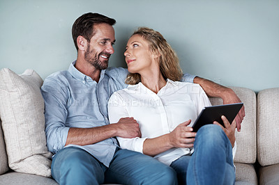 Buy stock photo Cropped shot of a couple using a tablet while relaxing on the sofa