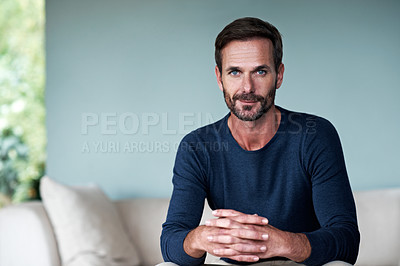 Buy stock photo Cropped portrait of a handsome man sitting on his living room sofa