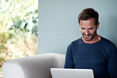 Buy stock photo Cropped shot of a handsome man using his laptop while sitting on the living room sofa