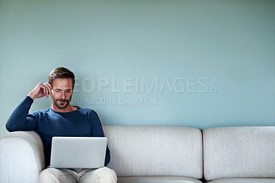 Buy stock photo Cropped shot of a handsome man using his laptop while sitting on the living room sofa