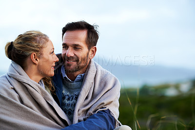 Buy stock photo Cropped shot of an affectionate couple wrapped in a blanket while sitting outdoors
