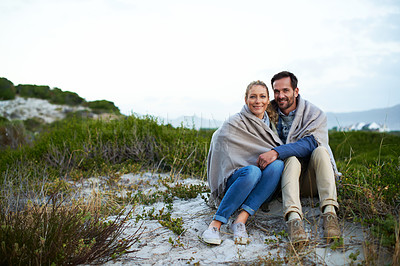Buy stock photo Full length portrait of an affectionate couple wrapped in a blanket while sitting outdoors