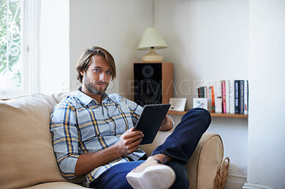 Buy stock photo Portrait of a young man using a digital tablet while sitting on a sofa at home
