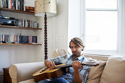 Buy stock photo Shot of a young man playing a guitar on the sofa while relaxing at home