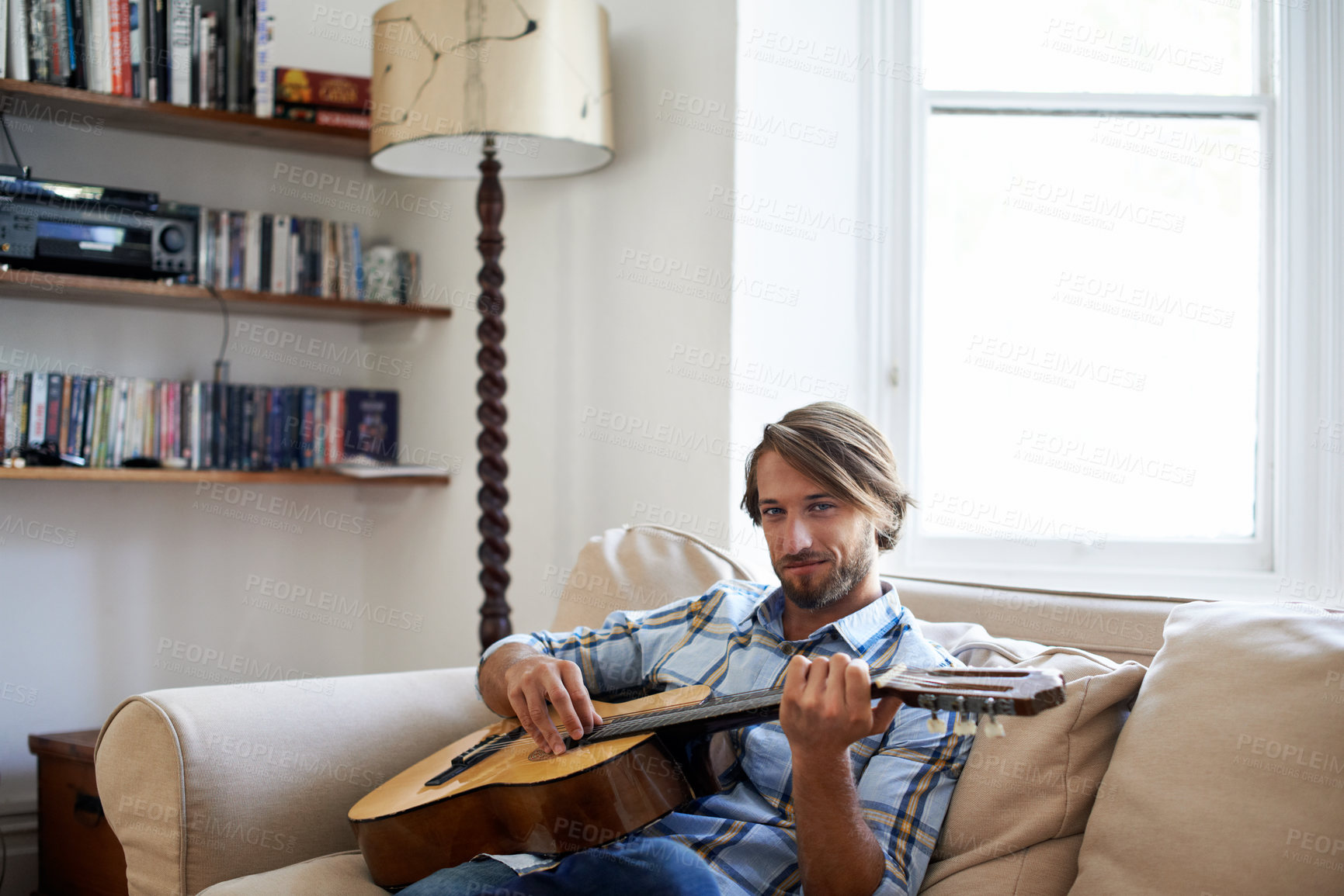Buy stock photo Shot of a young man playing a guitar on the sofa while relaxing at home