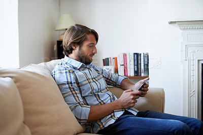 Buy stock photo Shot of a young man using a digital tablet while sitting on a sofa at home