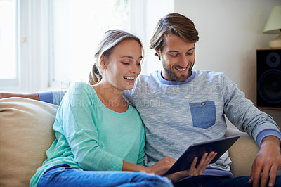Buy stock photo Shot of a young couple using a digital tablet while relaxing on a sofa at home