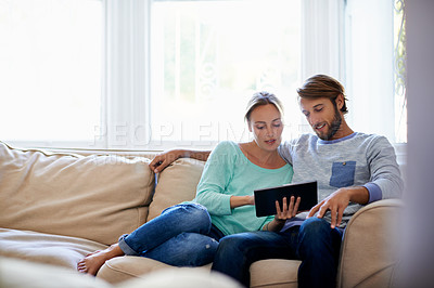 Buy stock photo Shot of a young couple using a digital tablet while relaxing on a sofa at home