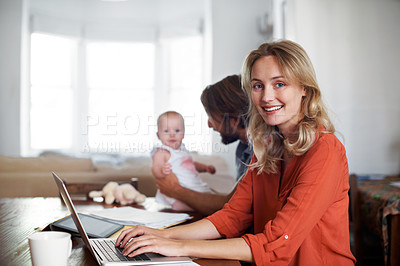 Buy stock photo Portrait of a mother using a laptop with her husband and baby in the background