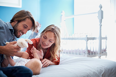 Buy stock photo Shot of a young couple playing with their baby on a bed