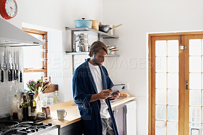 Buy stock photo Shot of a young man using a digital tablet in the kitchen in the morning