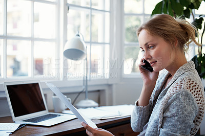 Buy stock photo Shot of a young woman talking on the phone while working on a laptop at home