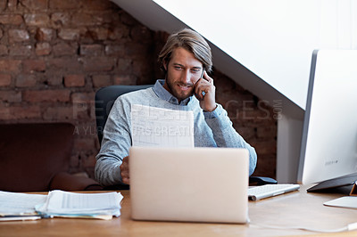 Buy stock photo Shot of a young man talking on the phone and reading paperwork while working on a computer at home