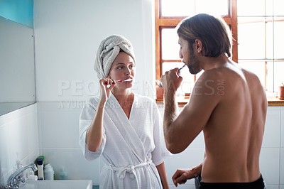 Buy stock photo Shot of a young couple brushing their teeth in the bathroom in the morning