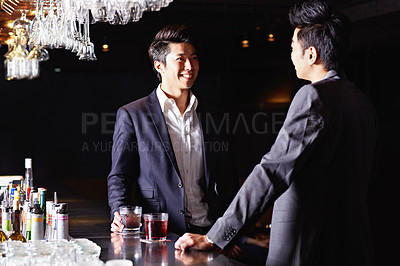 Buy stock photo Shot of a two male friends drinking and talking together in a nightclub