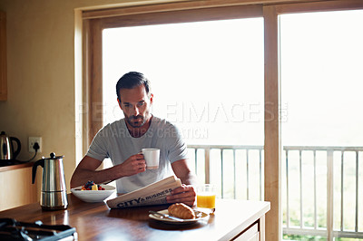 Buy stock photo Cropped shot of a handsome man eating breakfast while reading the newspaper