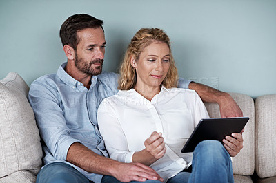 Buy stock photo Cropped shot of a couple using a tablet while relaxing on the sofa