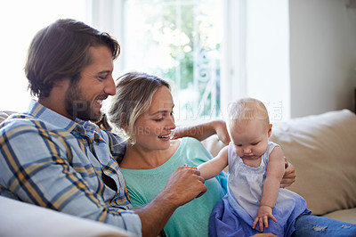 Buy stock photo Shot of a young couple sitting on the sofa at home with their baby daughter