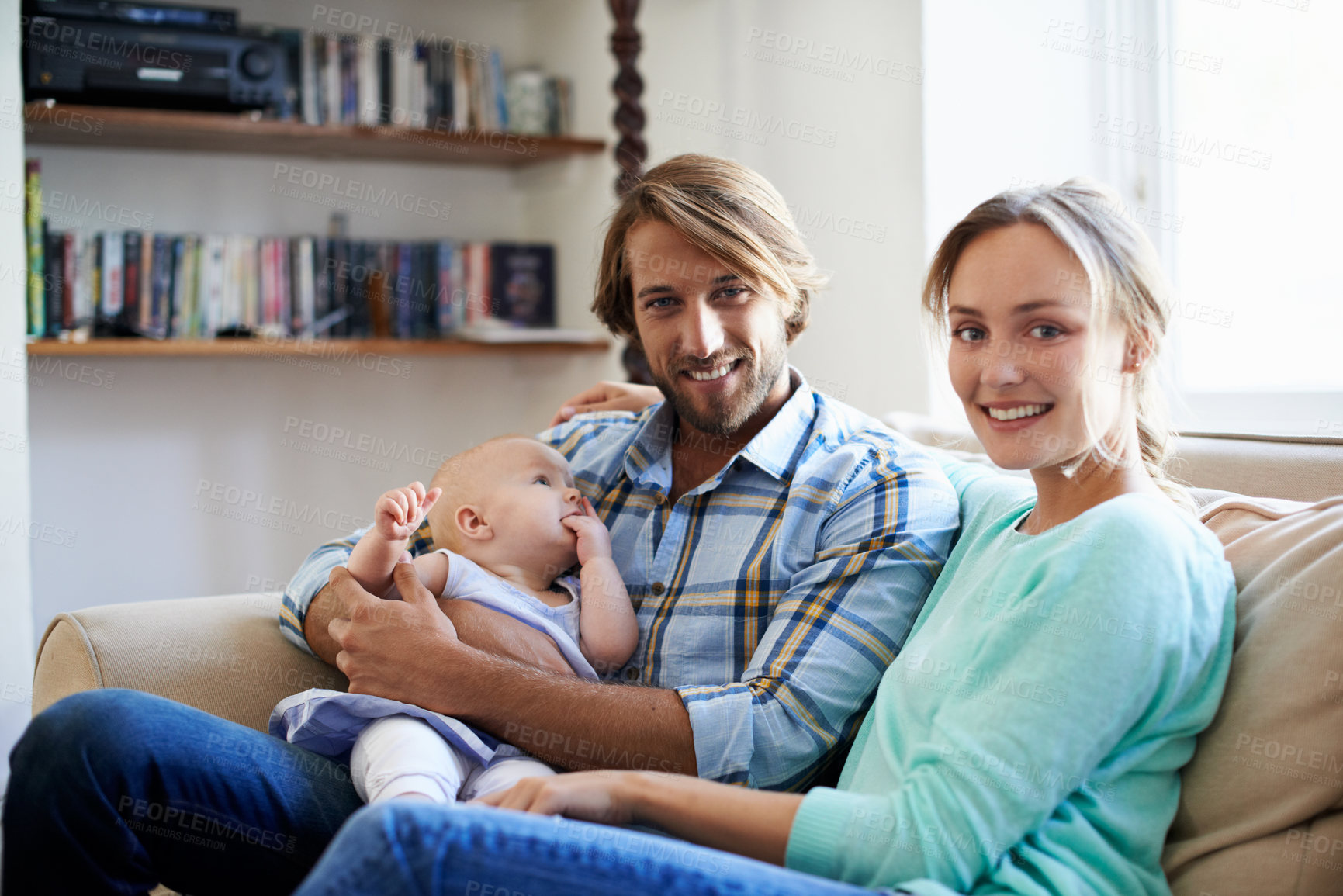 Buy stock photo Portrait of a young couple sitting on the sofa with their baby