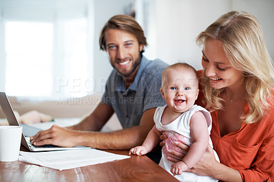 Buy stock photo Shot of a young man using a laptop while sitting with his wife and baby daughter