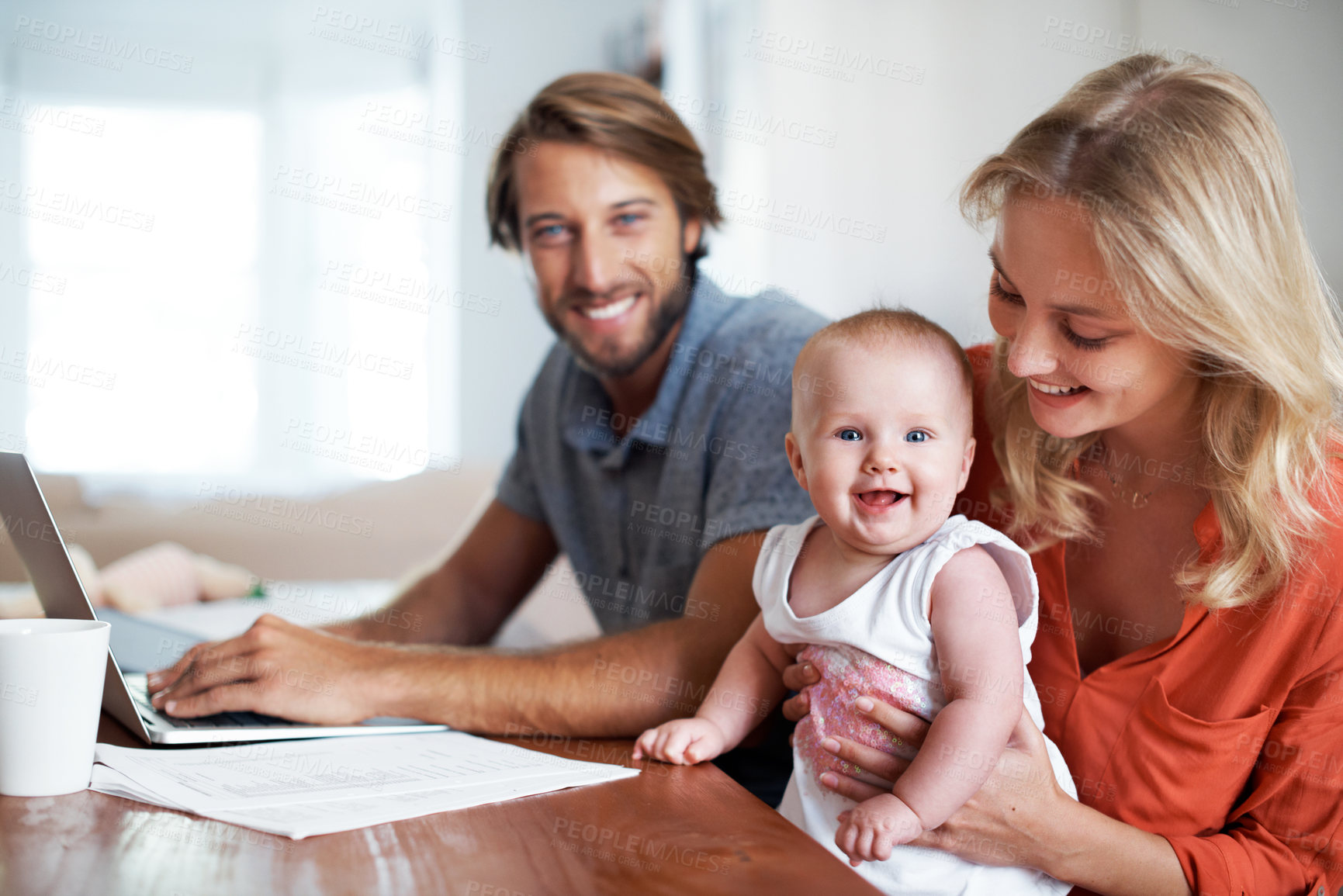 Buy stock photo Shot of a young man using a laptop while sitting with his wife and baby daughter