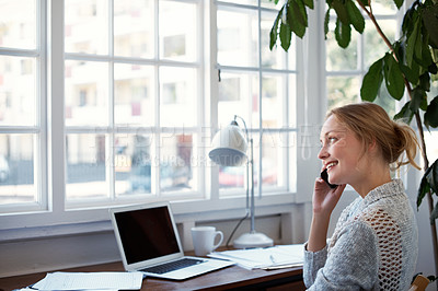 Buy stock photo Shot of a young woman talking on the phone while working on her laptop at home