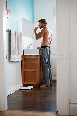 Buy stock photo Full length shot of a young man brushing his teeth in the bathroom