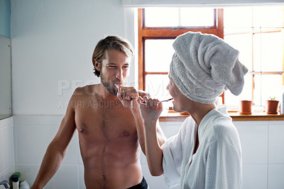 Buy stock photo Shot of a young couple brushing their teeth in the bathroom in the morning