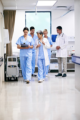 Buy stock photo Shot of a team of doctors walking and talking in a hospital corridor