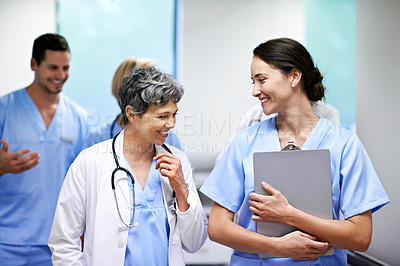 Buy stock photo Shot of a team of doctors walking and talking in a hospital corridor
