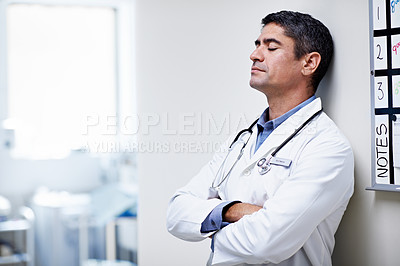Buy stock photo Shot of a tired doctor leaning against the wall in a hospital