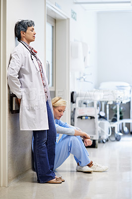 Buy stock photo Shot of two exhausted doctors leaning against the wall in a hospital