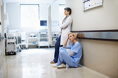 Buy stock photo Shot of two exhausted doctors leaning against the wall in a hospital