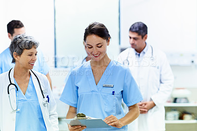 Buy stock photo Shot of a team of doctors walking and talking in a hospital corridor