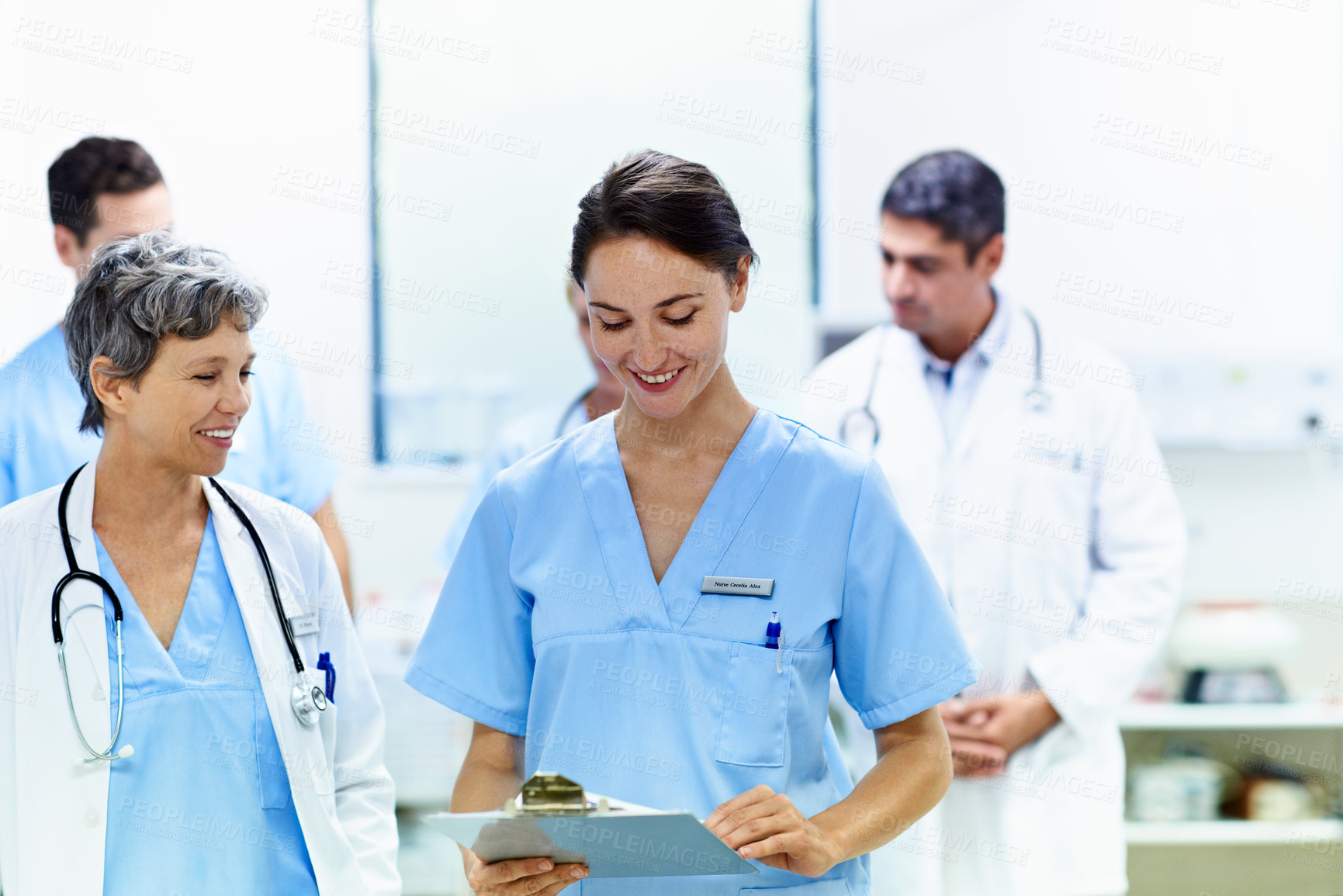 Buy stock photo Shot of a team of doctors walking and talking in a hospital corridor