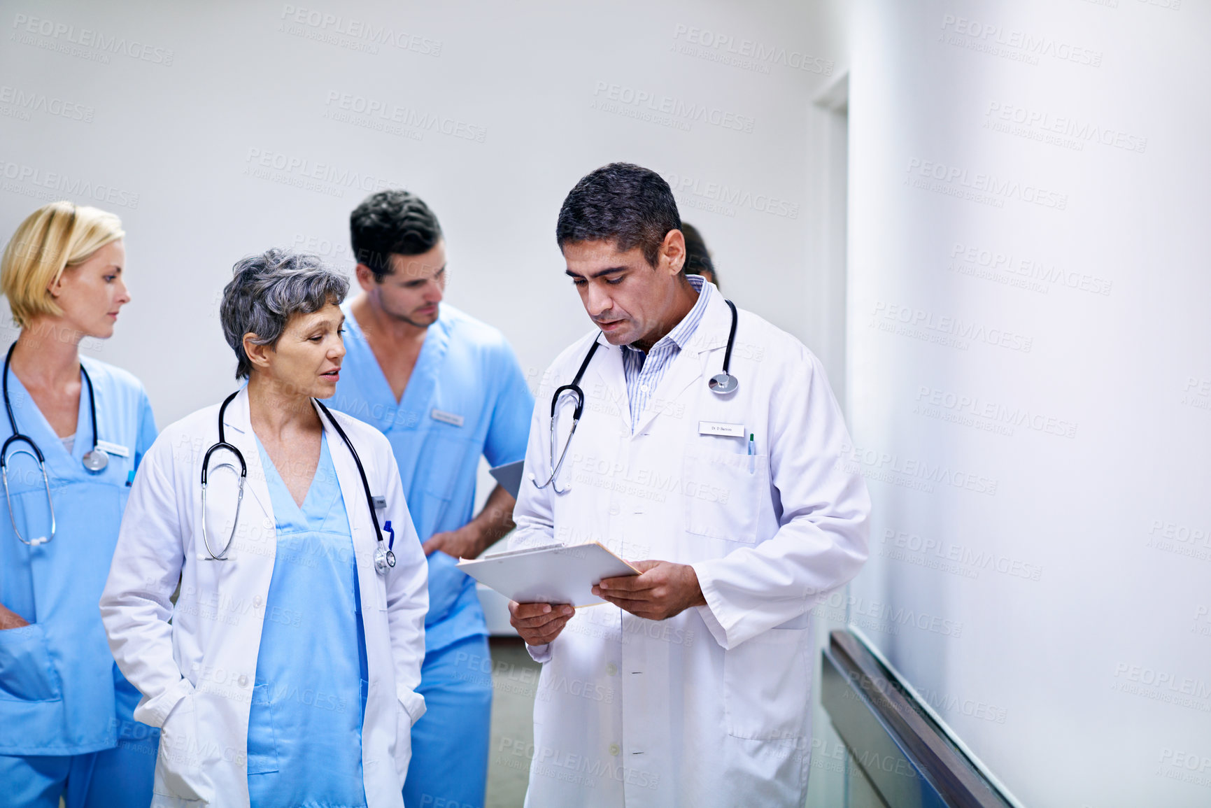 Buy stock photo Shot of a team of doctors walking and talking in a hospital corridor