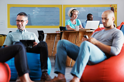 Buy stock photo Cropped shot of two businessmen sitting on beanbag chairs with colleagues in the background