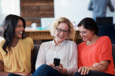 Buy stock photo Cropped shot of three businesswomen laughing while looking at a cellphone