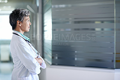Buy stock photo Shot of a thoughtful-looking doctor standing in a hospital corridor