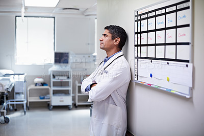 Buy stock photo Shot of a doctor standing by a shift schedule in a hospital